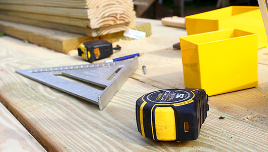 stainless steel triangular measurer beside tape measure and two yellow containers thumbnail