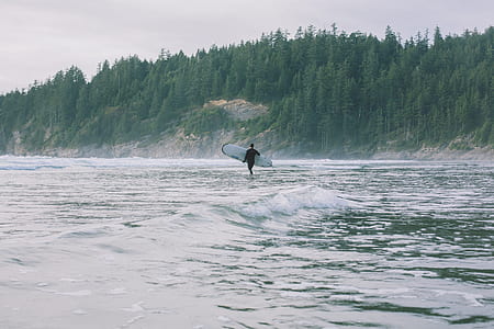 man carrying white surfboard on the sea during daytime photography thumbnail