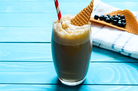 clear glass drinking cup filled with shake with waffle and straw beside towel on table thumbnail