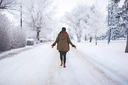 woman walking on snow-covered road during daytime thumbnail