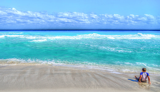 man wearing white and blue raglan shirt sitting in seashore facing the blue sea during daytime thumbnail