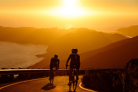 Two men on cycling exercises on bicycles on the coast at sunset thumbnail