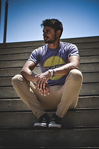 man wearing grey and yellow crew-neck t-shirt sitting on concrete stairway during daytime thumbnail