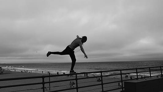 man balancing on railing near the beach thumbnail
