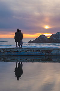 couple standing near body of water with their reflection on water thumbnail