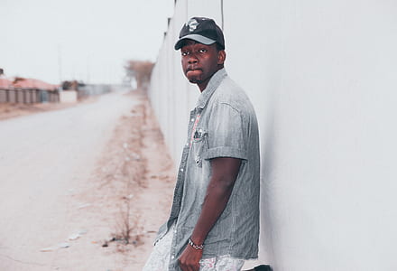 man stands beside white painted wall outdoor during day thumbnail