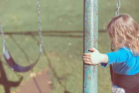 girl riding on black swing holding green and black metal post beside green grass field during daytime thumbnail