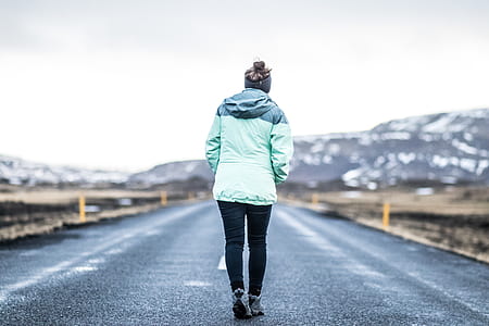 person wearing teal jacket while walking on road during daytime thumbnail
