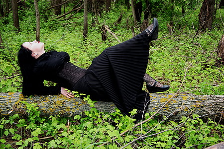 woman in black long-sleeved dress laying on tree trunk thumbnail
