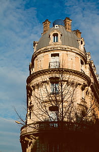 brown concrete building beside tree under white cloudy sky thumbnail