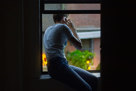 man sitting on window using smartphone thumbnail