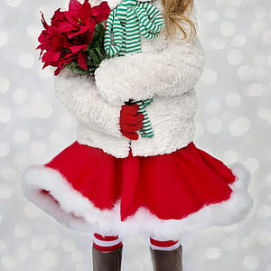 girl in white knit jacket and red mini skirt holding red poinsettia bouquet thumbnail