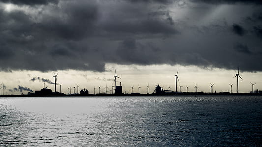 photo of silhouette of buildings during dark clouds daytime beside body of water thumbnail