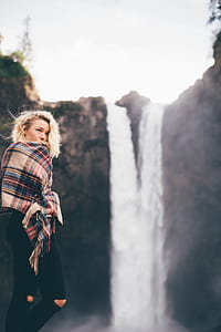 woman holding brown, red, and blue plaid scarf facing waterfalls thumbnail