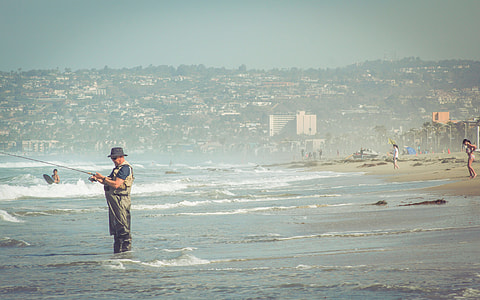 man in brown jumpsuit standing on beach while fishing thumbnail
