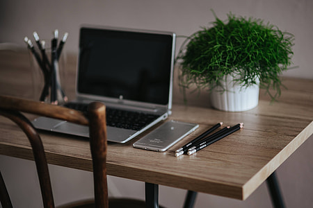 Silver Acer laptop on a wooden desk with a green plant, pencils and an Apple iPhone thumbnail