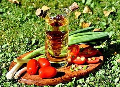 clear glass bottle, red tomatoes, and spring onions on top of oval brown wooden choppingboard thumbnail