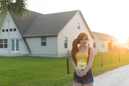 woman standing holding pokemon plush toy with the distance of white and gray house under white sky during daytime thumbnail
