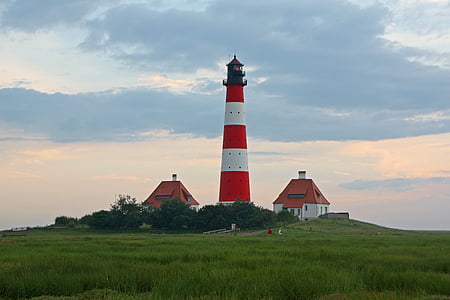 lighthouse between two house under cumulus cloud thumbnail