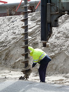 person bowing down in front of ground auger thumbnail