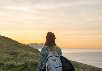 woman carrying backpack standing near cliff and body of water thumbnail