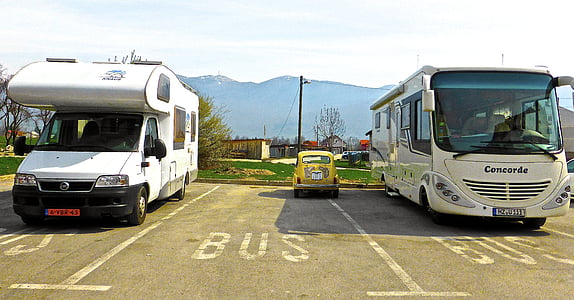 yellow Volkswagen Beetle coupe between two motorhomes on parking lot thumbnail