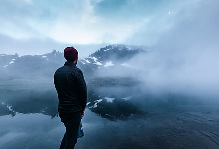 man standing on seashore with mountains nearby thumbnail