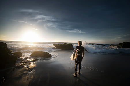 man holding bodyboard standing facing seashore thumbnail
