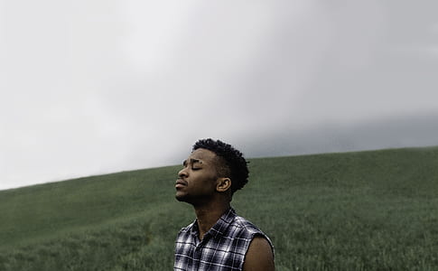 man wearing white, black, and grey plaid button-up sleeveless shirt standing on green grass field during daytime thumbnail