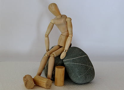 human shaped wooden toy sits on black stones thumbnail