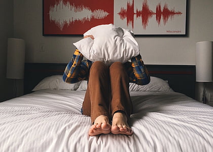 person wears teal, white, and brown long-sleeved shirt sits on white and gray stripe bed comforter thumbnail