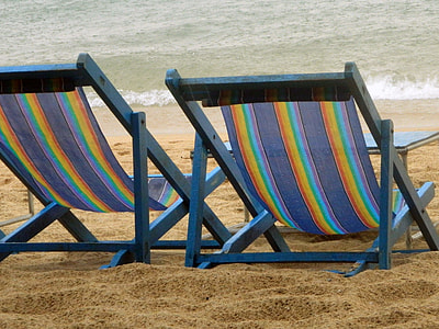 two blue lounge chairs on brown sand near body of water thumbnail