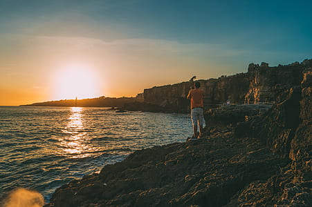 man standing in front of bod of water during sunset thumbnail