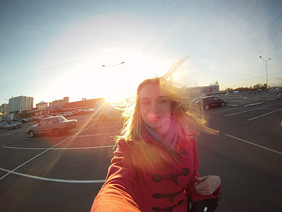 woman taking selfie while walking on parking lot near vehicle against sunlight thumbnail