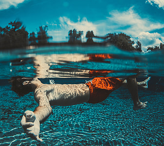man floating on body of water under white and blue sky thumbnail
