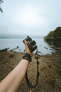 person holding camera near body of water thumbnail