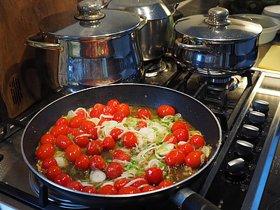 tomatoes and vegetables sauteed on black frying pan beside pots on gas range thumbnail