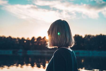 woman looking at distance of trees and body of water under blue and white sky thumbnail