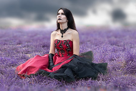 woman wearing red and black strapless dress sits on purple grass field at daytime thumbnail