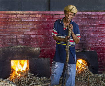 man stans holding stick near fireplace thumbnail