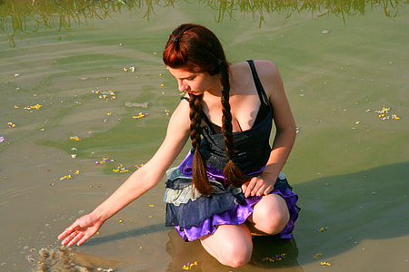 woman in black sleeveless dress sitting near body of water thumbnail