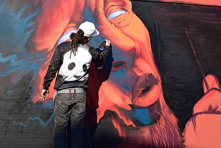 man drawing graffiti on wall during daytime thumbnail