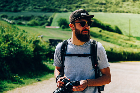 man standing behind green field holding DSLR camera thumbnail