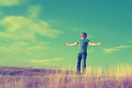 man in green crew-neck t-shirt ;blue denim jeans standing on brown grass field under blue sky photo thumbnail