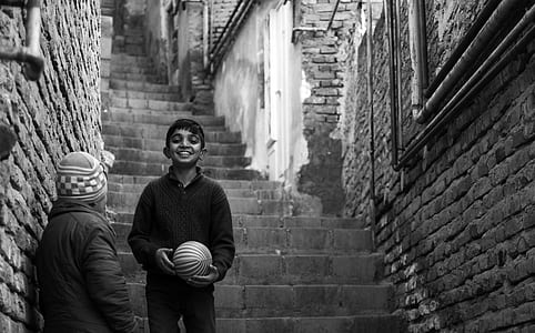 grayscale photography of boy holding ball on stairs thumbnail