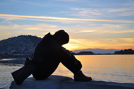 silhouette photo of person sitting down near body of water during sunset thumbnail