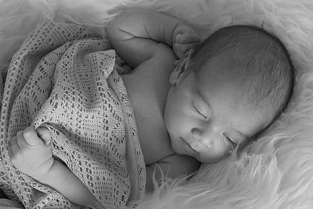 grayscale photography of a baby sleeping on white fur comforter thumbnail