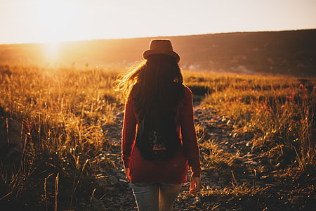 woman in red long-sleeved top waking in grass during golden hour thumbnail