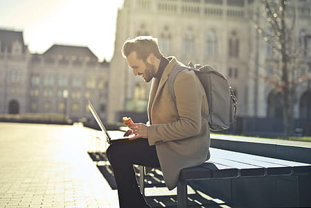 Young Adult bearded male backpacker with backpack on his shoulders, using a laptop while holding an ice cream cone thumbnail