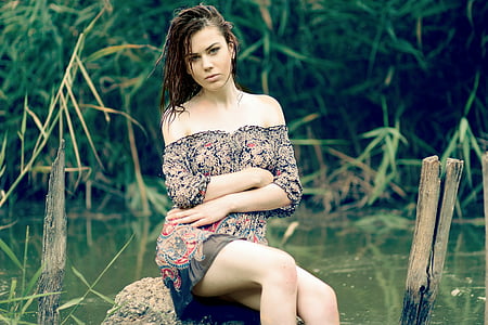 woman in floral off-shoulder top sitting on stone near river thumbnail